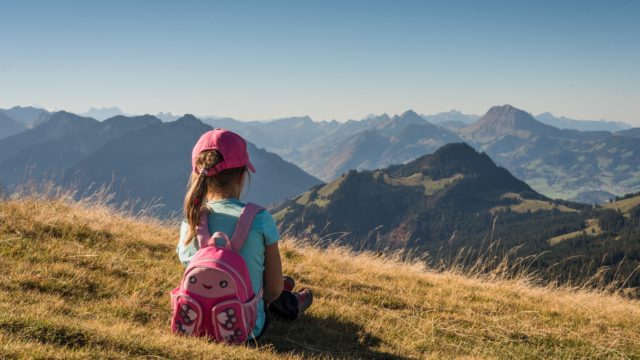 子供の女の子が草原でリュック背負って座っている-min